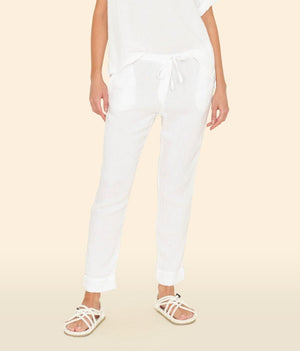 Person wears the Xirena Jordyn Pant—white cotton gauze pull-on pants with a drawstring waist—paired with a loose white top and white sandals, standing against a neutral background.