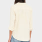 A person is seen from the back wearing the Xirena Scout Cotton Gauze Shirt in cream, featuring rolled cuffs and a shirttail hem, paired with light blue jeans.