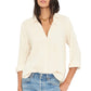 A woman wears the Xirena Scout Cotton Gauze Shirt in cream, featuring a lightweight button-front design, shirttail hem, and rolled sleeves, paired with light blue jeans against a plain background.