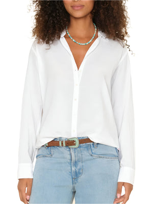 A person wearing the Xirena Beau Shirt, a menswear-inspired white cotton poplin button-up, paired with light blue jeans, a brown belt, and a turquoise bead necklace, standing with hands by their sides.