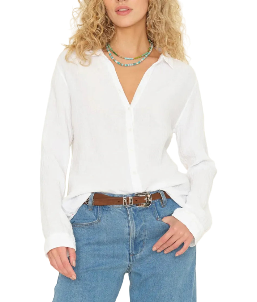 A person wearing the Xirena Scout Shirt, paired with blue jeans, a brown belt, and layered beaded necklaces.