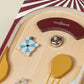 Close-up of the Coco Village Wooden Play Pinball Machine, inspired by classic circus arcade games, featuring a blue and white spinning wheel, a yellow balloon shape, a red curved bumper, and a silver ball on a light wood surface—this screen-free toy adds timeless fun to any playroom.