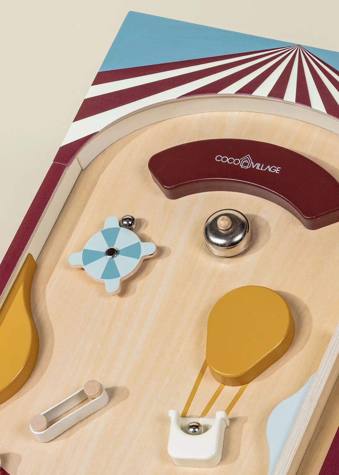 Close-up of the Coco Village Wooden Play Pinball Machine, inspired by classic circus arcade games, featuring a blue and white spinning wheel, a yellow balloon shape, a red curved bumper, and a silver ball on a light wood surface—this screen-free toy adds timeless fun to any playroom.