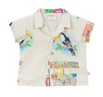 The Arsene & Les Pipelettes Baby Boys' Cocos Frios Collared Shirt features a playful design with colorful toucan and fruit cart illustrations on a light background. Made from comfortable cotton twill, it's the perfect addition to any child’s wardrobe.