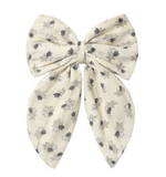 The Rylee & Cru Girls’ Oversized Bow features long tails and a beige background decorated with a delicate pattern of small black and gray flowers. This charming accessory is finished with an alligator clip for secure and easy styling.
