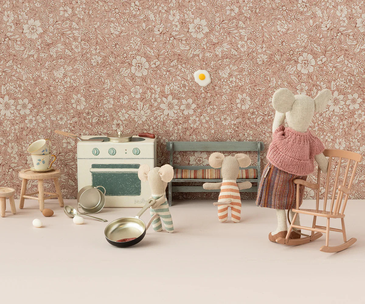 A family of fabric mice, including a mother and three children, are play-pretending to cook in the Maileg Cooking Set, Mouse by Maileg, featuring pots, pans, kitchen utensils, and an egg against a floral-patterned wallpaper backdrop.