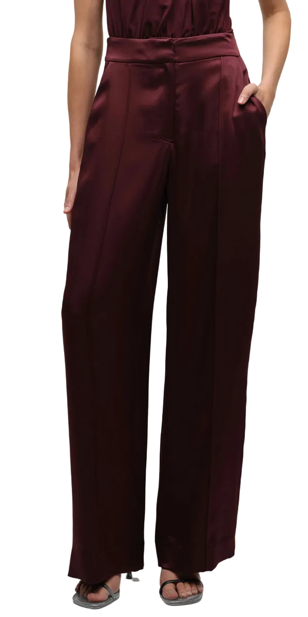 Someone wearing the Simkhai Kyra Wide Leg Pant, featuring a high-waisted fit and tailored waistband, with hands in pockets and open-toe sandals.