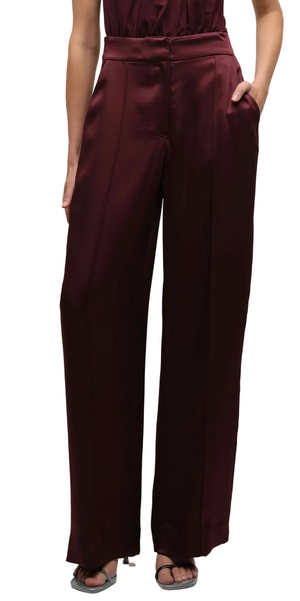 Someone wearing the Simkhai Kyra Wide Leg Pant, featuring a high-waisted fit and tailored waistband, with hands in pockets and open-toe sandals.
