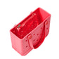 A rectangular pink Bitty Bogg® Bag by Bogg Bags, featuring signature holes and an included transparent zippered pouch, is displayed from an angled top view. This compact tote is ideal for organizing your essentials and can be easily washed for extra convenience.