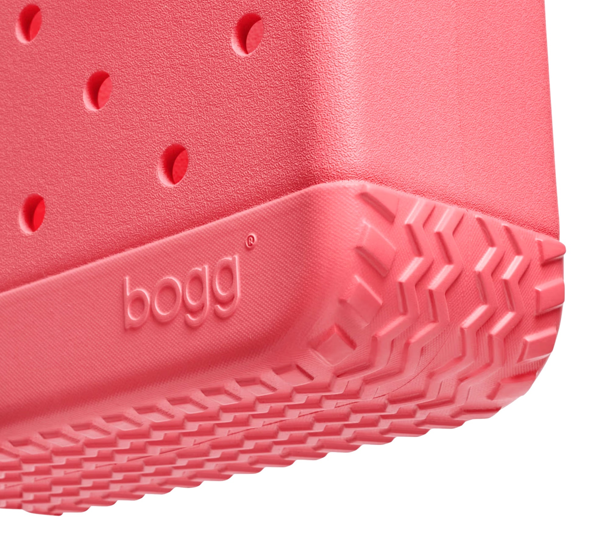 Close-up of the corner of a pink, textured rubber Bitty Bogg® Bag by Bogg Bags, featuring the embossed “bogg” logo and ventilation holes above a treaded bottom—highlighting this stylish, washable compact tote.