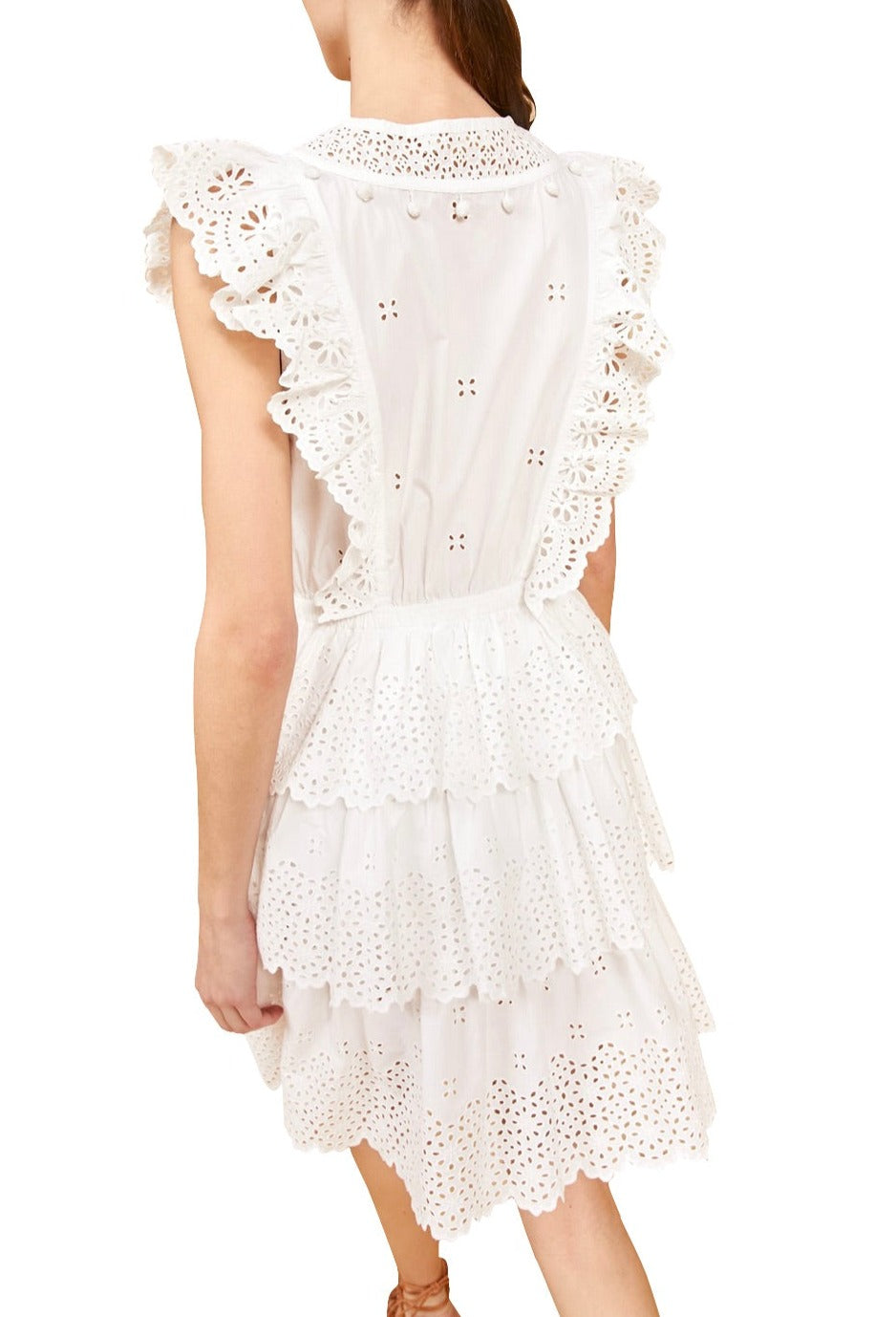 Rear view of a woman wearing a white sleeveless Ulla Johnson Lilith Dress with geometric eyelets and ruffled tiers, standing against a plain background.