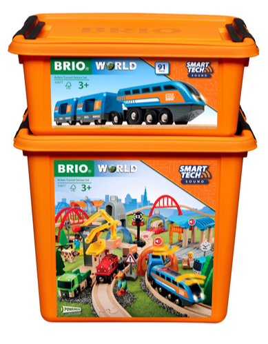 Two orange storage boxes containing the BRIO World Action Tunnel Deluxe Set, packed with a blue train and a vibrant track featuring Smart Tech Sound for enhanced railway excitement, complete with an Action Tunnel for thrilling adventures.