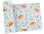 The Angel Dear Swaddle Blanket is a light blue bamboo baby blanket featuring brown footballs, play diagrams, "GO TEAM" flags, and arrows—a soft and cozy choice for little sports fans.