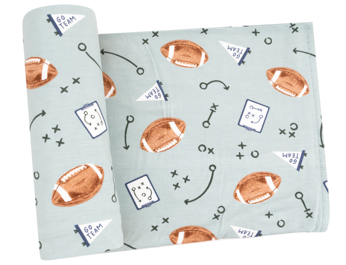 The Angel Dear Swaddle Blanket is a light blue bamboo baby blanket featuring brown footballs, play diagrams, "GO TEAM" flags, and arrows—a soft and cozy choice for little sports fans.