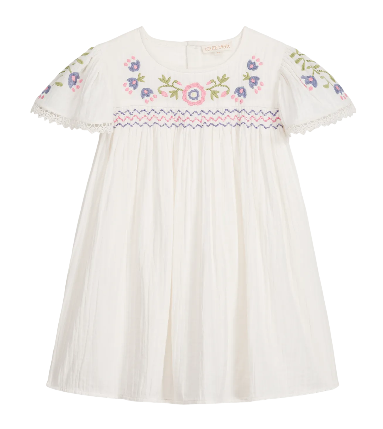 The Girls’ Ana Dress by Louise Misha is a white cotton dress with short sleeves, adorned with colorful floral embroidery on the chest and sleeves, hand-smocked details along the embroidered yoke, pink and blue zigzag trim, and finished with delicate lace edging on the sleeves.