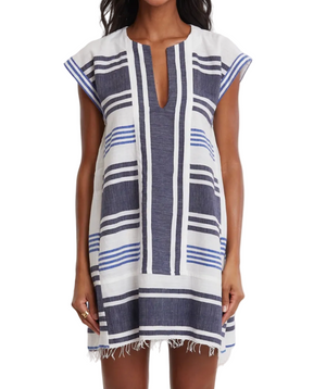 A woman wears the Lemlem Elina Caftan, a hand-woven cotton Ethiopian dress with short sleeves, knee-length cut, blue and white stripes, and a frayed hem.