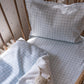 A crib with a plush toy rests under the Picnic Gingham Blue Crib Sheet by Gooselings, featuring soft, OEKO-TEX certified cotton sateen.