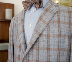 A mannequin showcases men's luxury clothing with a light blue shirt, a patterned brown bow tie, and the Samuelsohn Super Light Blazer in gray plaid, reflecting superior craftsmanship by Samuelsohn.