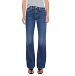 A person wearing Mother’s The Bookie Twist Skimp bootcut jeans in a light blue wash and black open-toe sandals, standing against a plain light background.