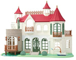 The Calico Critters Red Roof Riverside Manor is a white and light gray castle-style house featuring red roofs, green window frames, a balcony, and a small patio with a tub and faucet on the right side, all set atop a grassy base.