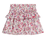 The Girls’ Roumia Skirt by Louise Misha is a short, ruffled skirt made from lightweight cotton veil, showcasing a pink, red, and green floral pattern on a white background. It features a smocked waistband and a layered design.