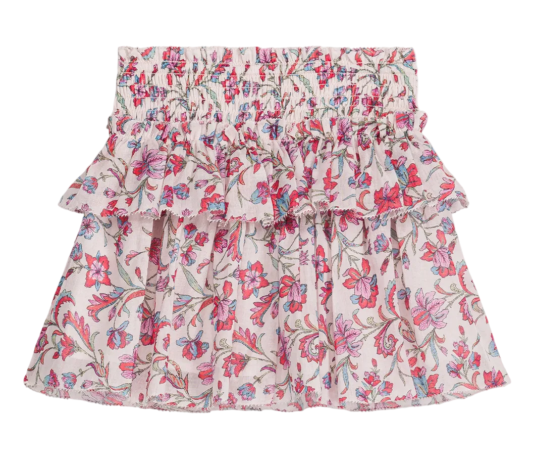 The Girls’ Roumia Skirt by Louise Misha is a short, ruffled skirt made from lightweight cotton veil, showcasing a pink, red, and green floral pattern on a white background. It features a smocked waistband and a layered design.