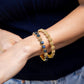 A person wearing two gold bracelets by Juliska Capucine De Wulf on their left wrist—including the Berry Gem Hinged Bangle—styled with a dark top and light jeans.