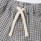 Close-up of the Quincy Mae Baby Boys’ and Boys’ Giovani Pant, showcasing a gray and white checkered woven gauze design with an elastic waistband, adjustable drawstring, and two brown buttons.