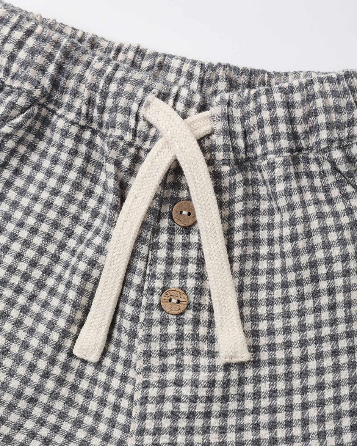 Close-up of the Quincy Mae Baby Boys’ and Boys’ Giovani Pant, showcasing a gray and white checkered woven gauze design with an elastic waistband, adjustable drawstring, and two brown buttons.