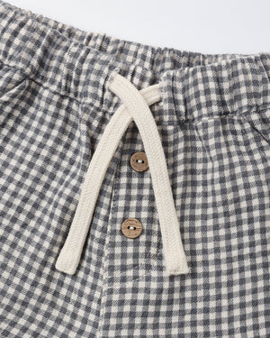 Close-up of the Quincy Mae Baby Boys’ and Boys’ Giovani Pant, showcasing a gray and white checkered woven gauze design with an elastic waistband, adjustable drawstring, and two brown buttons.