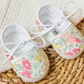 Baby Girls’ Liberty Fabric Espadrille Slipper by Tartine et Chocolat, featuring white laces and a pastel floral pattern, displayed on a textured woven mat beside cream-colored fabric.