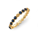 The Berry Gem Hinged Bangle by Juliska Capucine De Wulf features alternating blue gemstone cabochons and small gold bead clusters, showcasing regal gem-drop elegance on a white background.