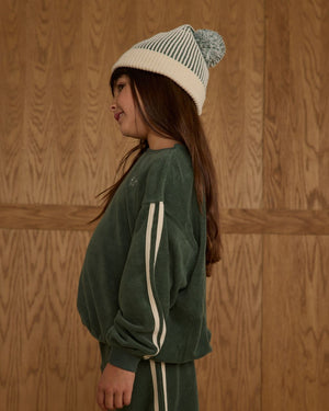 A young girl in the Rylee & Cru Baby Girls' and Girls' Oversized Sweatshirt stands in profile against a wooden backdrop, showcasing cozy style.
