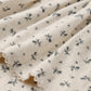 Close-up of a cream-colored fabric from the Quincy Mae Baby Girls’ Pointelle Skirted Bodysuit, featuring small black insect or dragonfly motifs, scalloped edges, a delicate peplum skirt, and snap button closures.