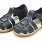 L'Amour Shoes Boys' Aiden Fisherman Sandal features black waxed leather, closed toe, buckled ankle strap, and tan rubber soles that develop a unique patina over time.
