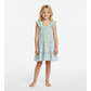 A young child with long blond hair stands barefoot against a plain white background, wearing the Mer Girls' Paloma Dress, which features smocked flutter sleeves and a ruffle twirly skirt.