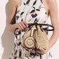 A woman in a sleeveless, floral dress holds Stella McCartney’s Falabella Crochet Raffia Bucket Bag, a small beige luxury vegan accessory with a brown leather strap and circular woven detail, echoing the brand's signature tote style.