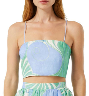 A woman is wearing the Rhode Dina Top by Rhode, a sleeveless linen crop top with spaghetti straps, showcasing a blue and green abstract floral pattern.