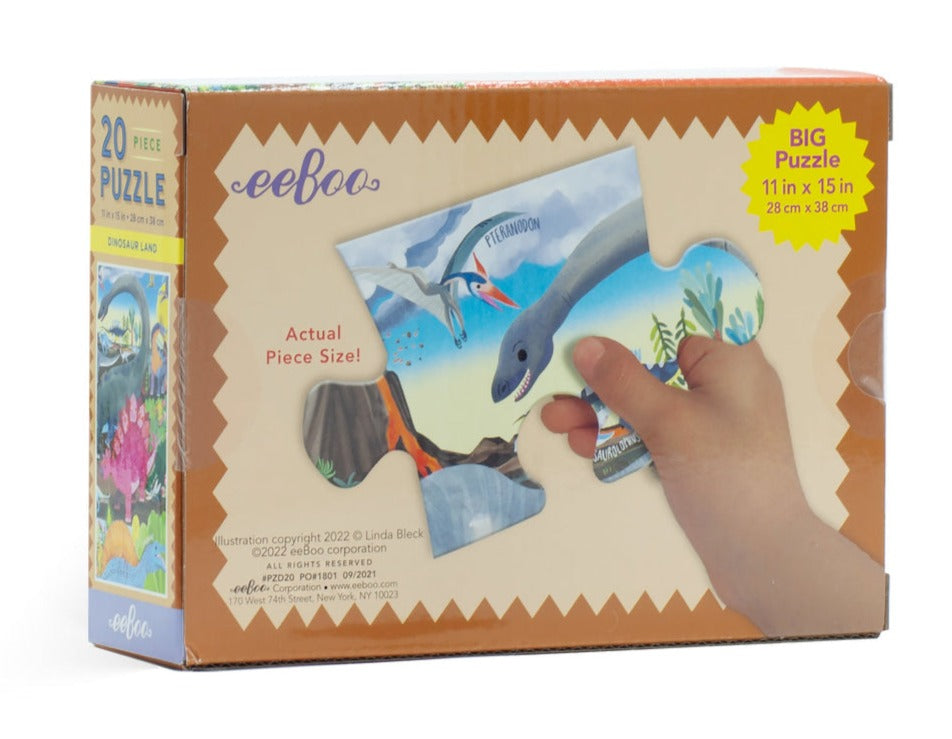 The eeboo Dinosaur Land 20 Piece Puzzle by Eeboo, measuring 11" x 15", features a hand holding a plesiosaur piece to show the "Actual Piece Size." It's ideal for improving hand-eye coordination while delving into a colorful prehistoric setting.