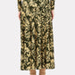 A person shown from the back against a white background wears the Ulla Johnson Fiona Jersey Skirt, which features a gold floral pattern on dark fabric that creates the illusion of a high-waisted skirt, styled with tan socks and black pointed-toe heels.