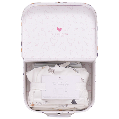 The Nesting Box Baby Take Home Set by Pink Chicken features an open suitcase with a chicken pattern, folded organic pima cotton fabric, and a card—making it a perfect newborn gift.
