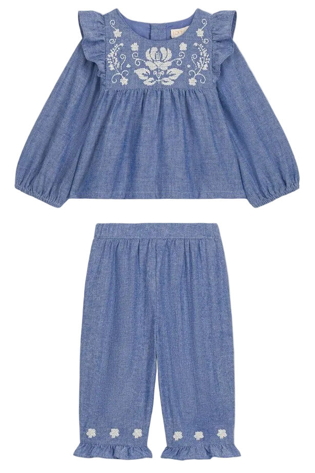 The Louise Misha Baby Girls’ Mikani Set is a charming two-piece toddler outfit, showcasing a cotton Oxford design with a long-sleeve blue top embellished with delicate white floral embroidery, paired beautifully with matching blue pants featuring an elastic waist and embroidered hem details for a coordinated look.