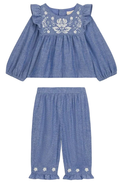 The Louise Misha Baby Girls’ Mikani Set is a charming two-piece toddler outfit, showcasing a cotton Oxford design with a long-sleeve blue top embellished with delicate white floral embroidery, paired beautifully with matching blue pants featuring an elastic waist and embroidered hem details for a coordinated look.