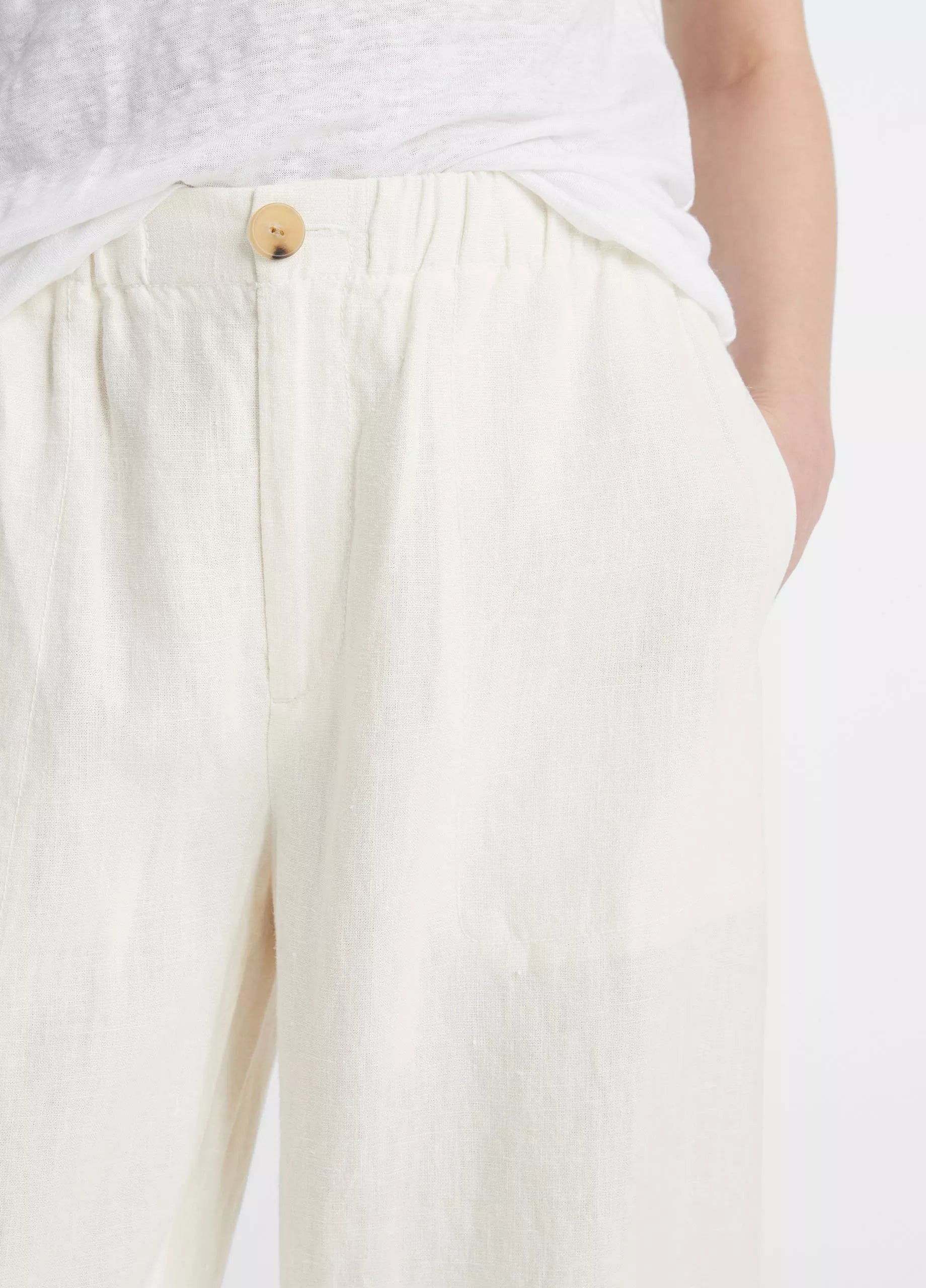 A person wears vince’s Hemp Utility Pant in breathable off-white linen-hemp with a wooden button, hands in pockets, and pairs it with a tucked-in white shirt for a relaxed silhouette.
