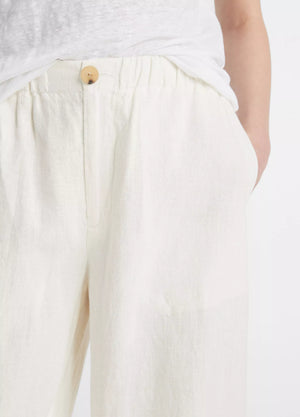 A person wears vince’s Hemp Utility Pant in breathable off-white linen-hemp with a wooden button, hands in pockets, and pairs it with a tucked-in white shirt for a relaxed silhouette.