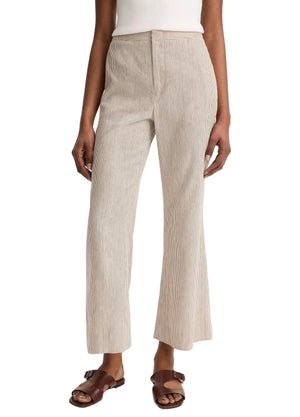 A person wearing Vince's Low Rise Ticking Striped Crop Flare Trouser, a white top, and brown sandals stands with arms relaxed at their sides.