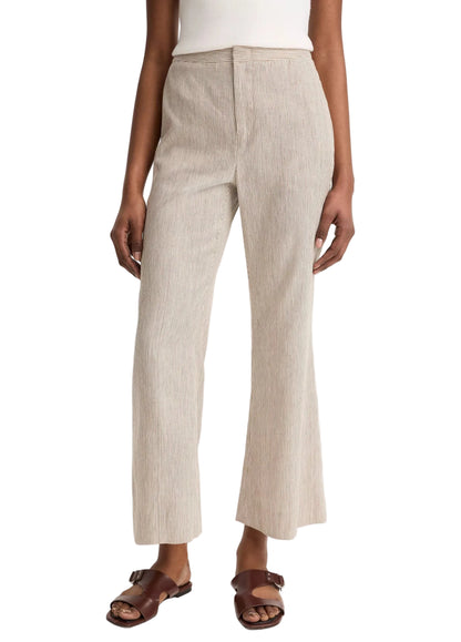 A person wearing Vince's Low Rise Ticking Striped Crop Flare Trouser, a white top, and brown sandals stands with arms relaxed at their sides.