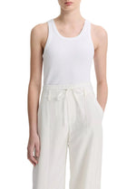 A person wearing the vince Ribbed Scoop Neck Tank in white and high-waisted white pants with a tie belt, standing against a plain background.