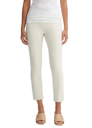 A person wearing the vince Bobbi Mid Rise Pant in a light-colored, straight-leg silhouette crafted from luxurious Italian cotton-blend ponte, paired with a white sleeveless top and beige slide sandals, stands against a plain background.