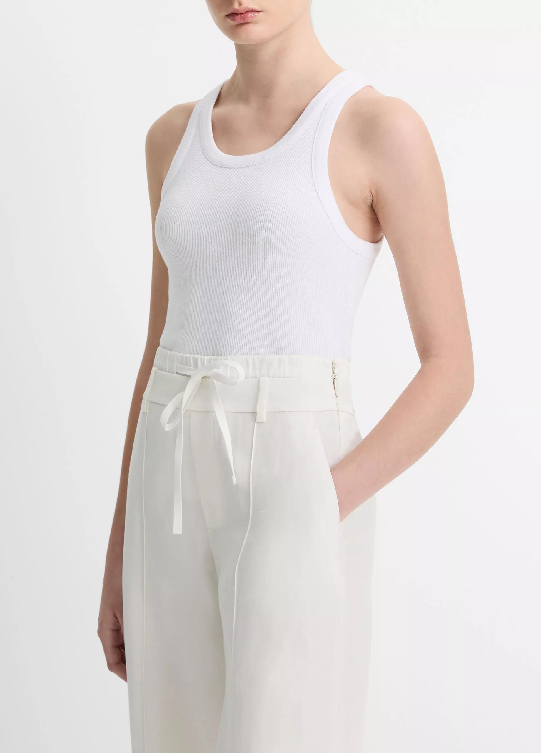 A person is wearing the vince Ribbed Scoop Neck Tank—a white, finely ribbed tank top made from a soft cotton modal blend—paired with high-waisted white drawstring pants, standing against a plain background.